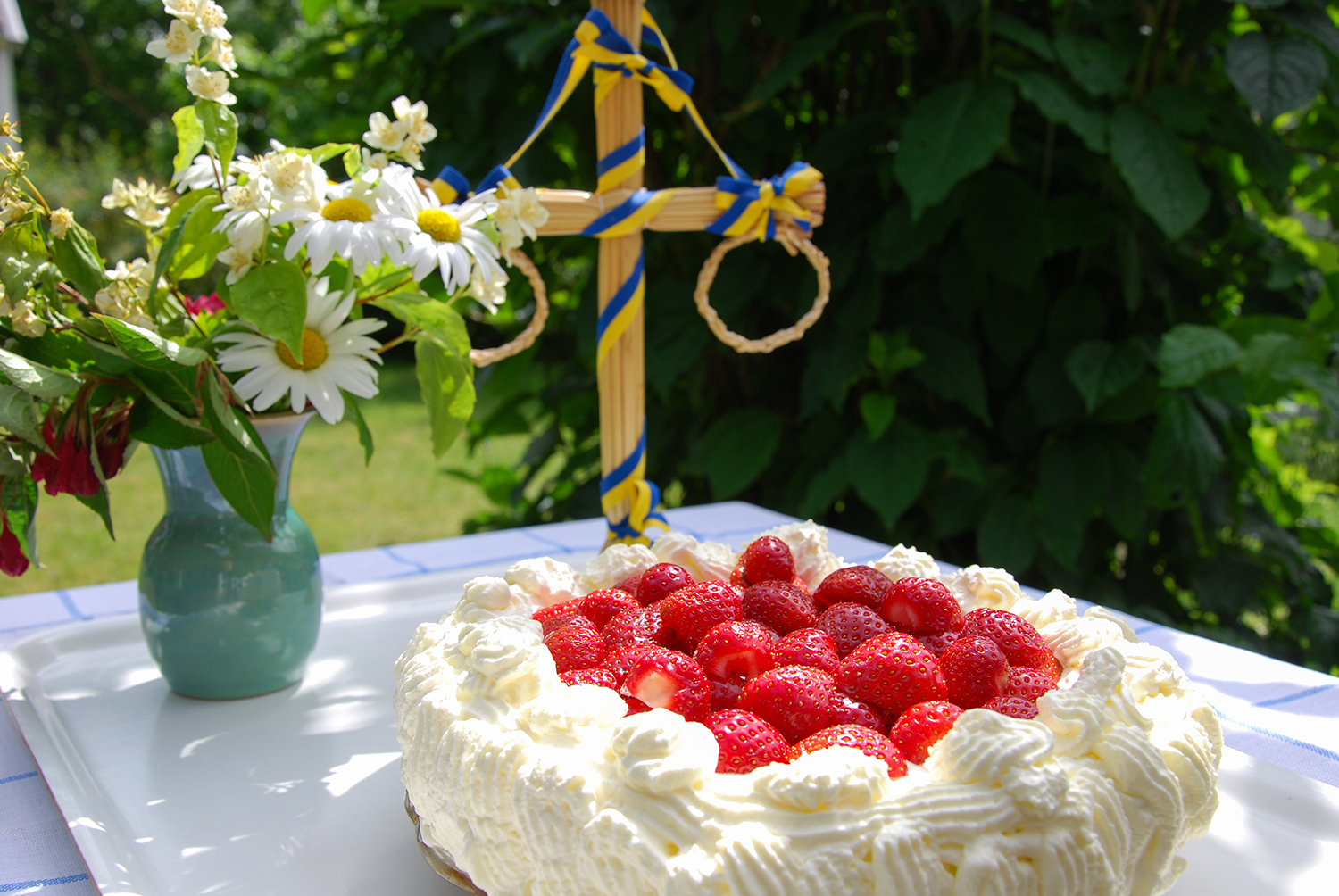 Bild på en jordgubbstårta som står på ett bord med blommor